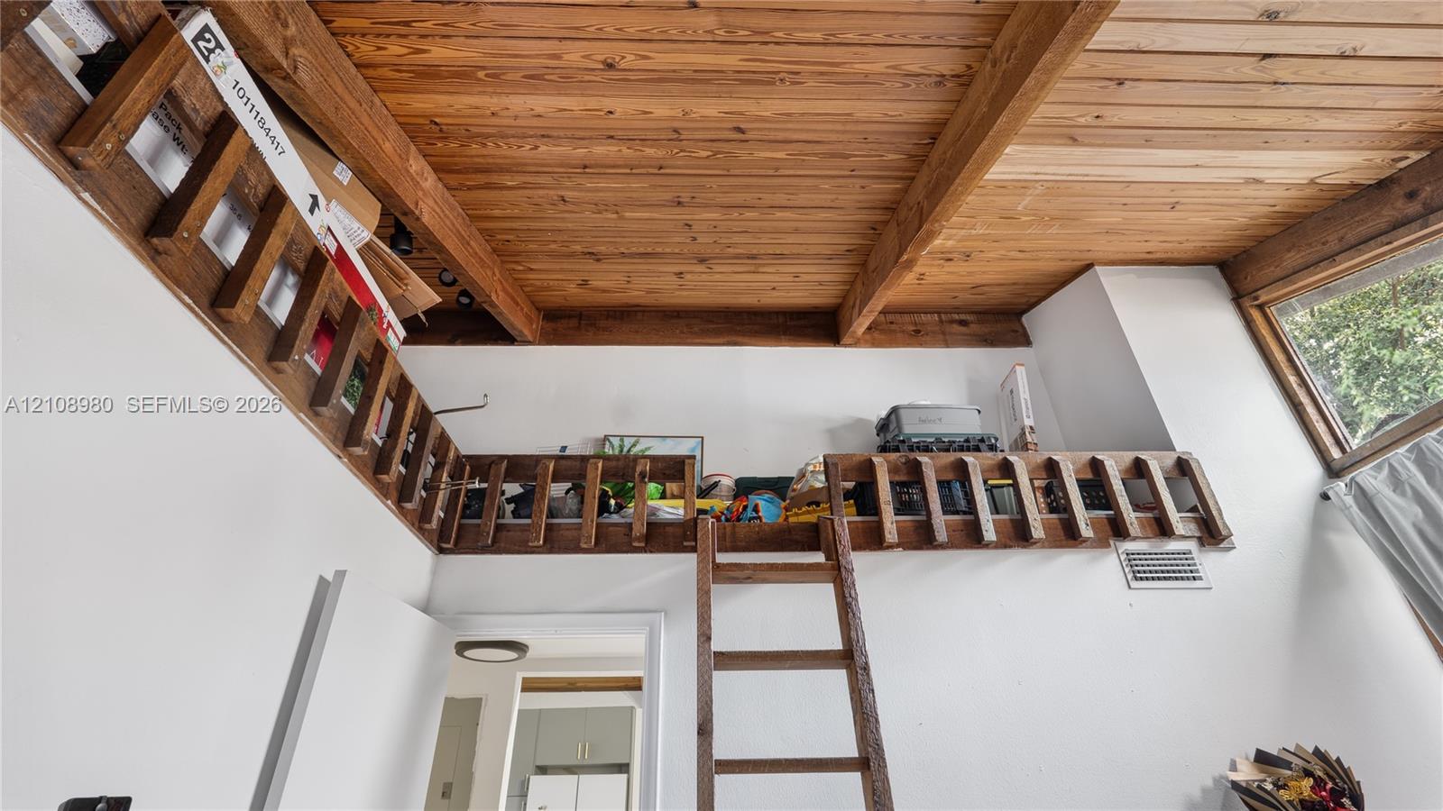 Interior space featuring high ceilings with exposed wood beams and wood-plank ceiling finish, an elevated wooden loft platform with integrated wood railings, and a wooden ladder