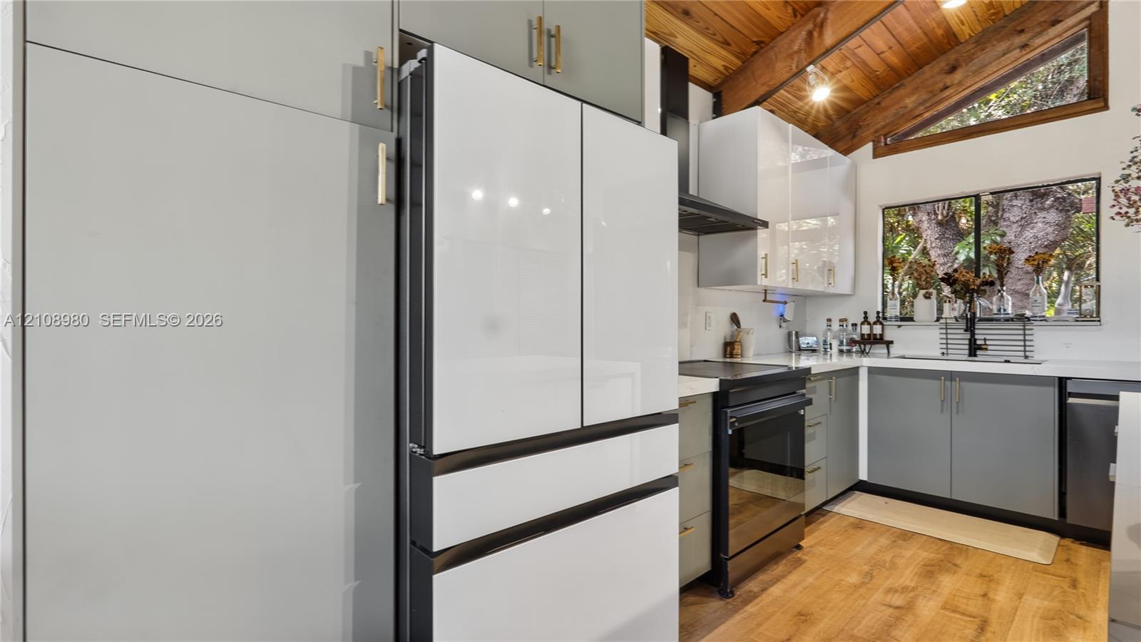 Kitchen featuring two-tone cabinetry with metallic hardware, integrated refrigerator, exposed wood-beam vaulted ceiling, and wood-finish flooring