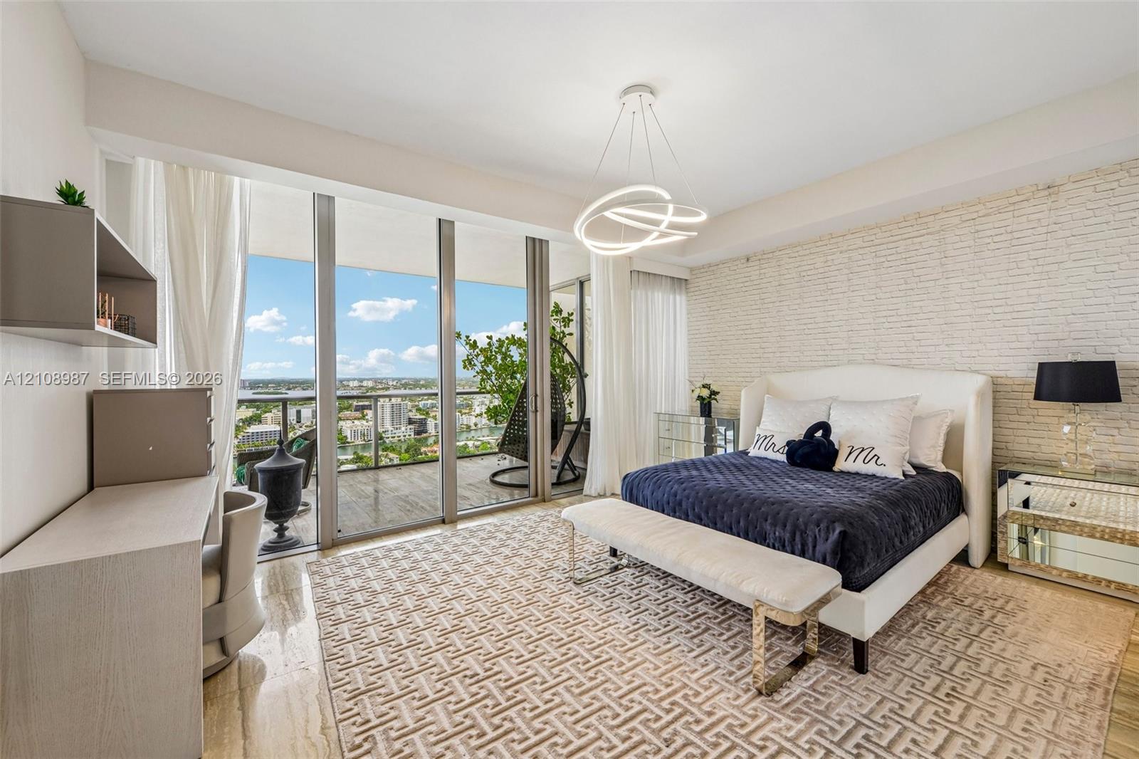Floor-to-ceiling glass sliding doors, textured brick accent wall, polished stone flooring, custom contemporary light fixture, and private balcony