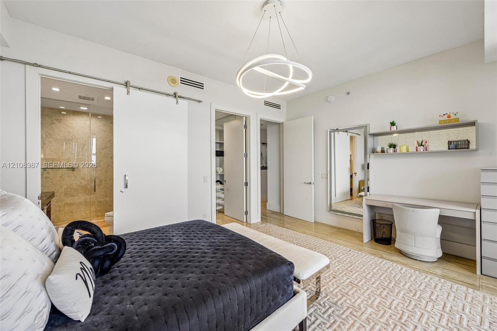 Contemporary architectural space featuring a stainless steel sliding barn door, minimalist circular LED pendant lighting, built-in wall-mounted desk with integrated shelving, and neutral wood-finish flooring
