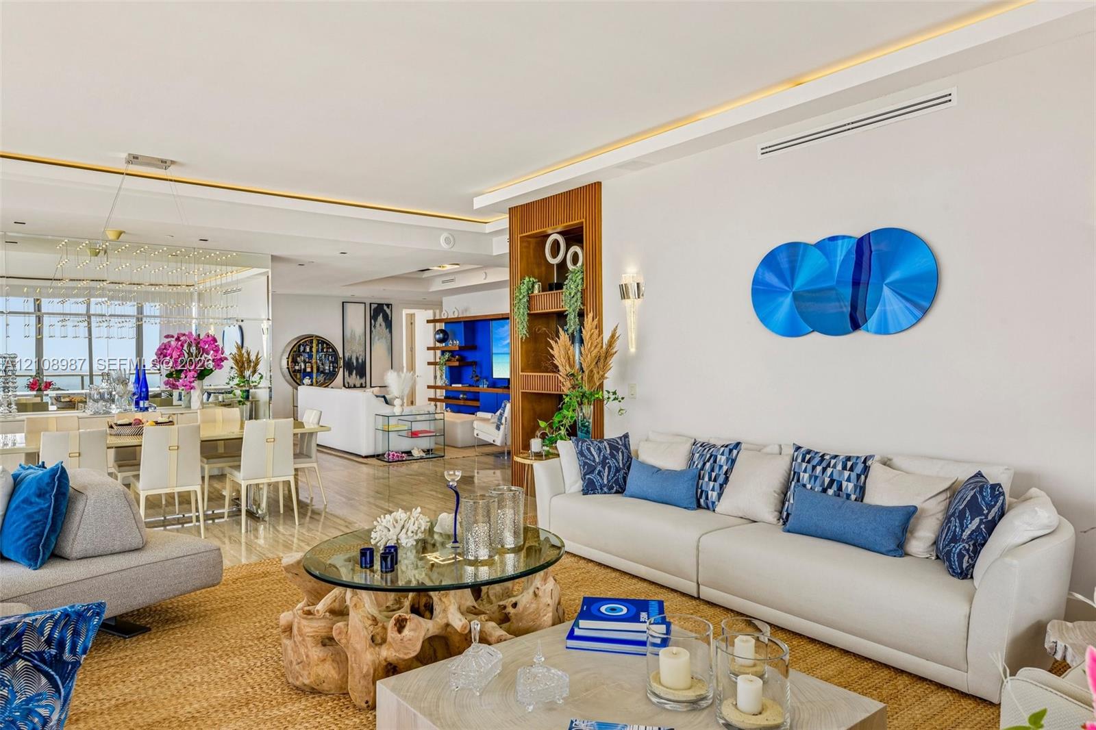 Open-concept interior featuring recessed cove lighting, built-in floor-to-ceiling wood shelving, mirrored wall paneling, and wood-finish flooring Open-concept interior featuring recessed cove lighting, built-in floor-to-ceiling wood shelving, mirrored wall paneling, and wood-finish flooring