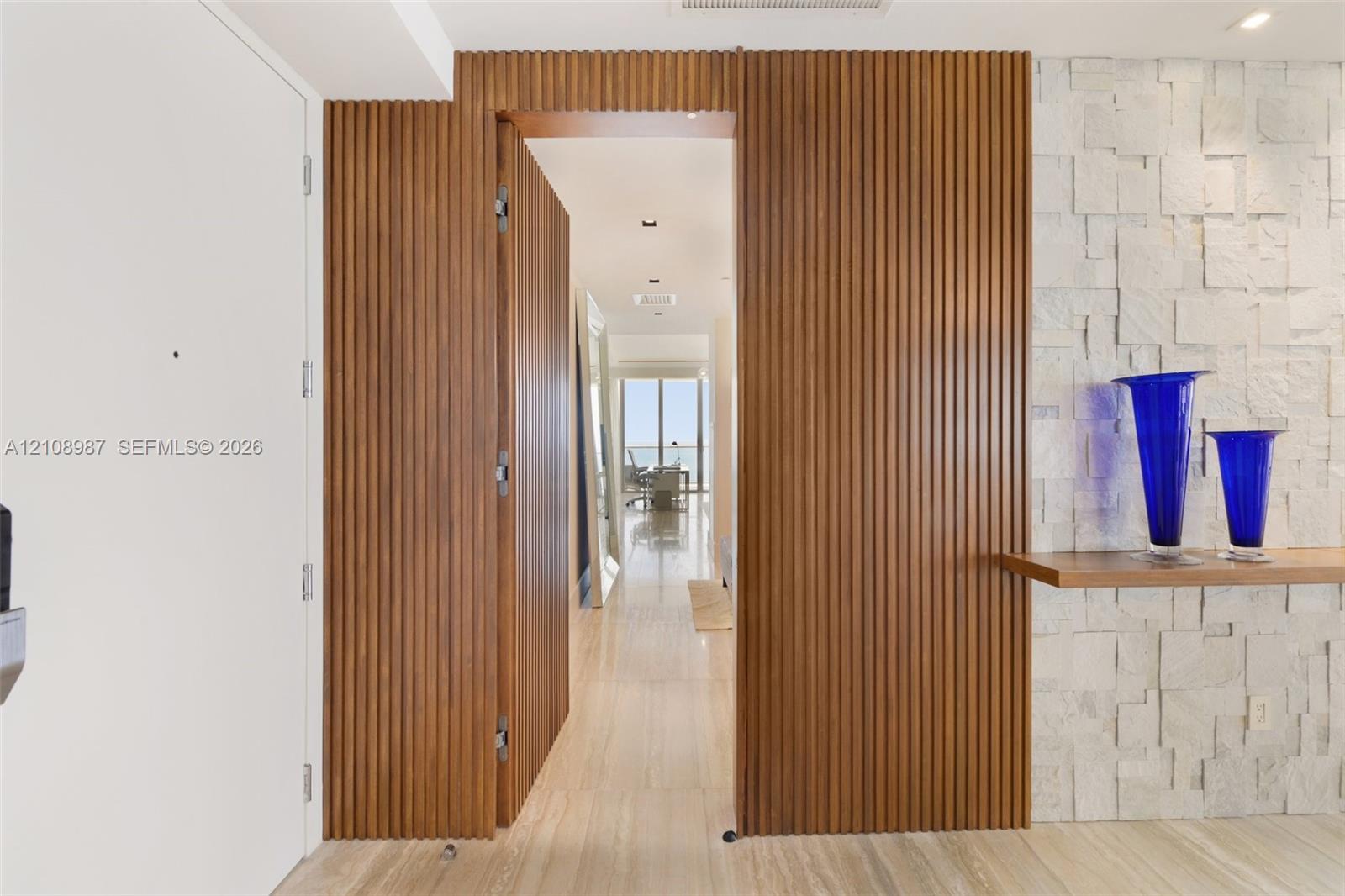 Floor-to-ceiling slatted wood wall paneling with an integrated door, textured natural stone accent wall, and polished stone flooring