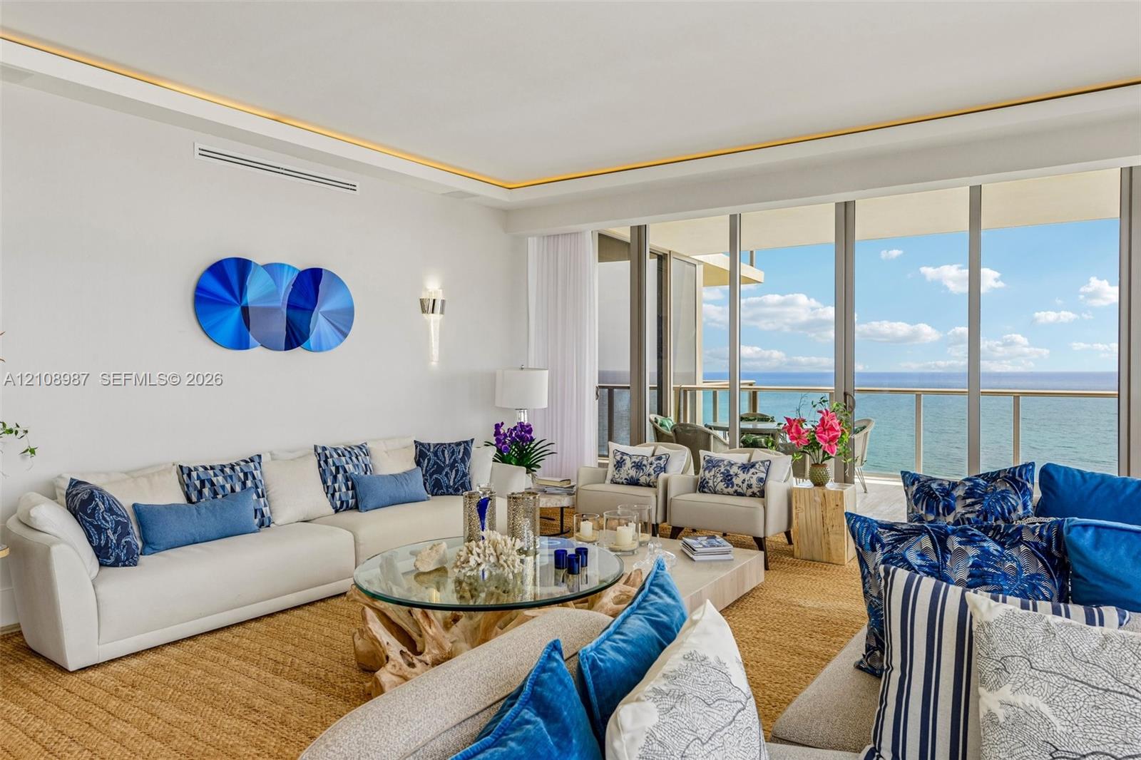 Living area featuring floor-to-ceiling glass sliding doors, recessed tray ceiling lighting, and integrated wall sconces Living area featuring floor-to-ceiling glass sliding doors, recessed tray ceiling lighting, and integrated wall sconces