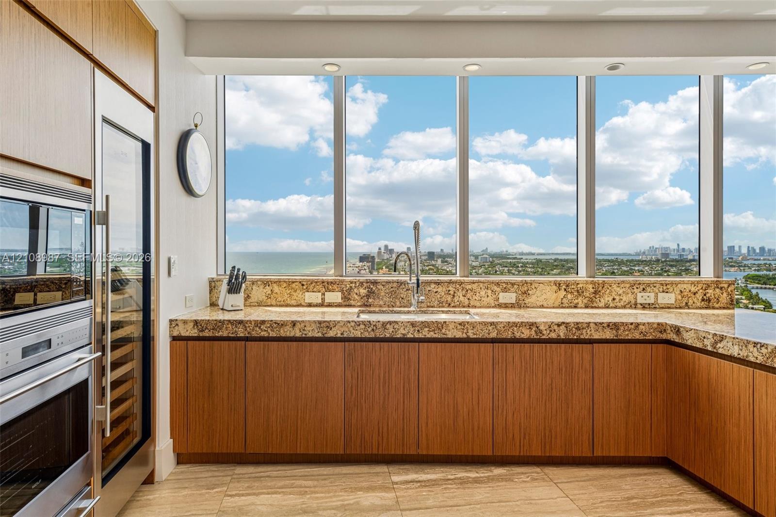 Kitchen featuring wood-finish cabinetry, stone countertops, floor-to-ceiling windows, built-in stainless steel double ovens, and a dual-zone wine refrigerator