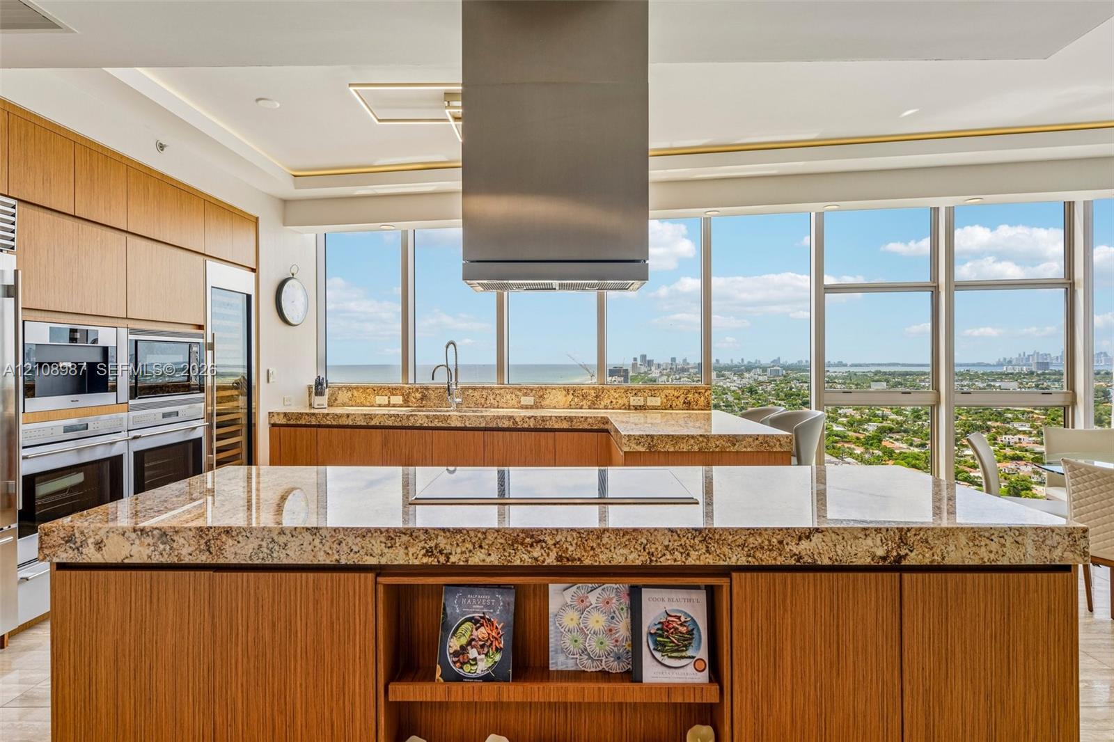 Kitchen featuring expansive stone countertops, floor-to-ceiling windows, stainless steel range hood, integrated wall oven and microwave, and wood cabinetry