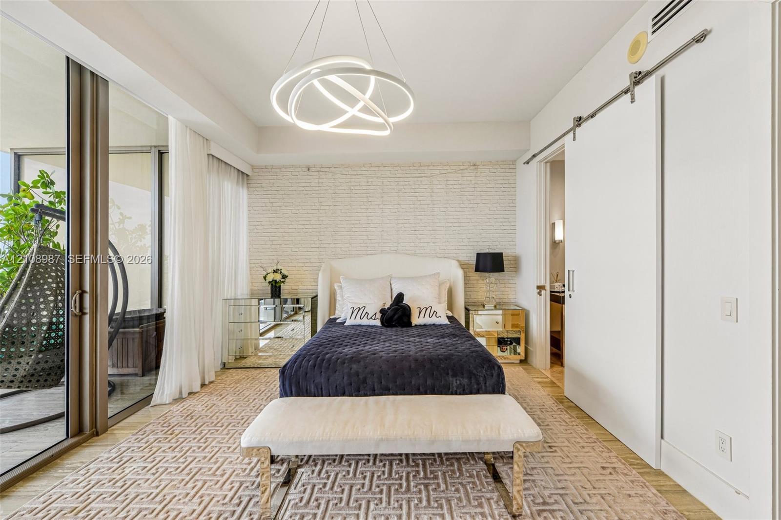 Textured brick accent wall, sculptural circular LED chandelier, floor-to-ceiling glass sliding doors, and white sliding barn door