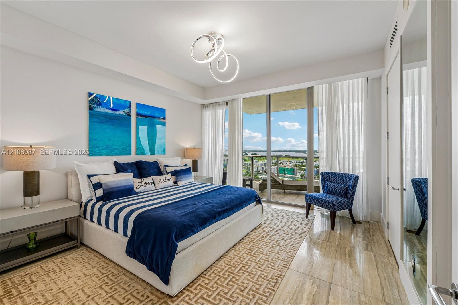 Floor-to-ceiling sliding glass doors, natural stone flooring, modern geometric LED chandelier, and a private balcony