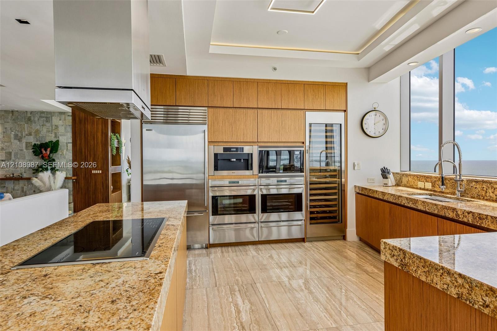 Chef-grade kitchen featuring custom wood-finish cabinetry, natural stone countertops, integrated stainless steel appliances, a built-in wine refrigerator, and polished stone flooring