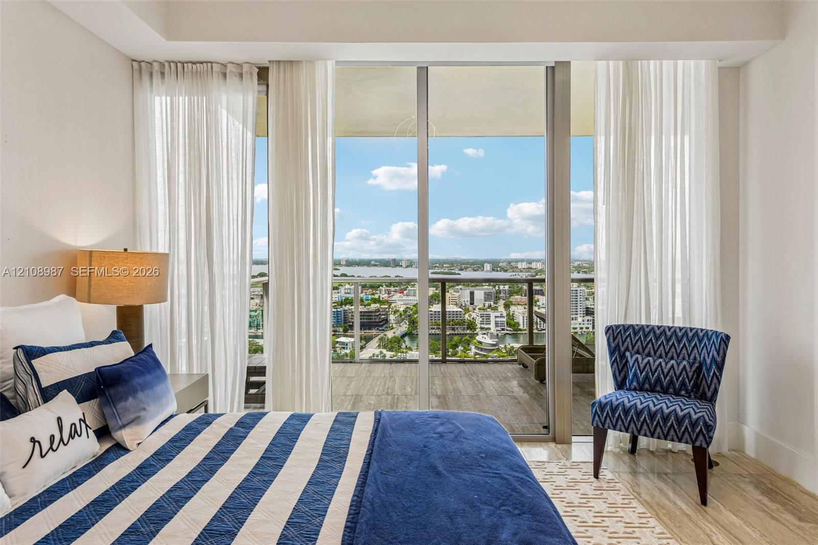 Floor-to-ceiling glass sliding doors opening to an expansive balcony, stone-finish flooring, and cityscape water-front scenery