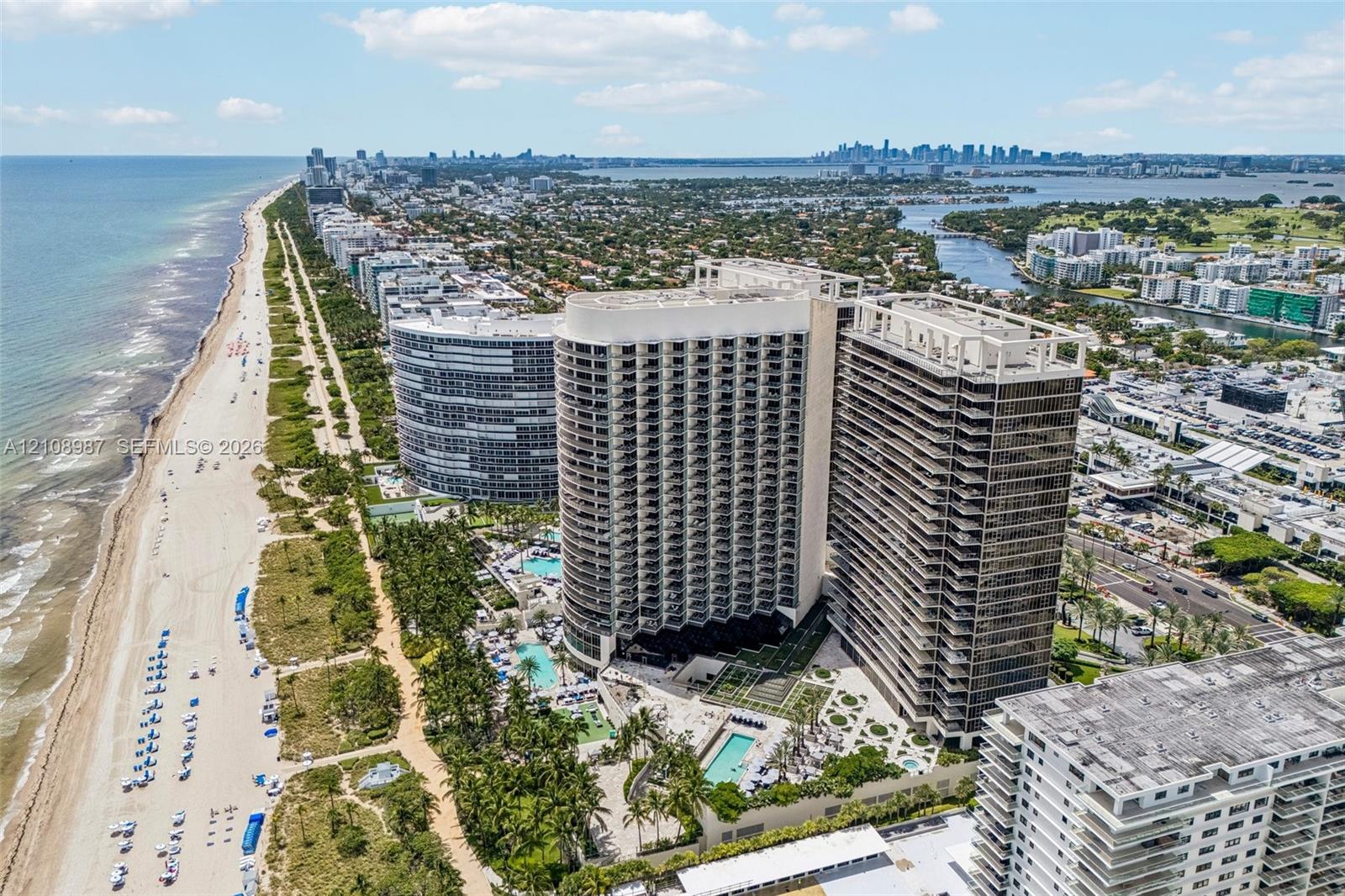 High-rise waterfront property featuring extensive balcony levels, an outdoor swimming pool, manicured grounds, and direct oceanfront positioning