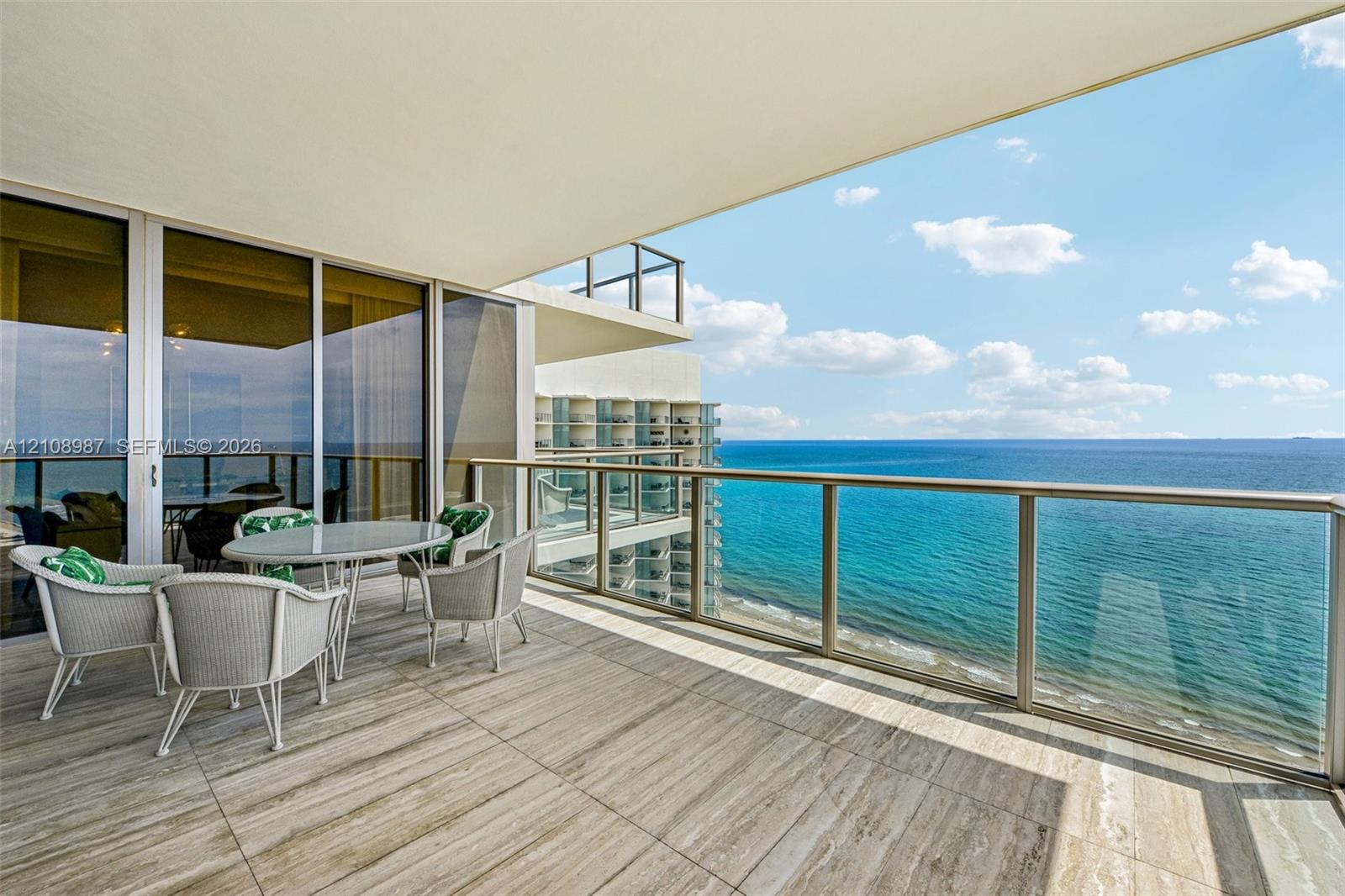 Covered balcony featuring large-format stone-finish tile flooring, floor-to-ceiling glass sliding doors, and a metal railing with a glass panel insert Covered balcony featuring large-format stone-finish tile flooring, floor-to-ceiling glass sliding doors, and a metal railing with a glass panel insert