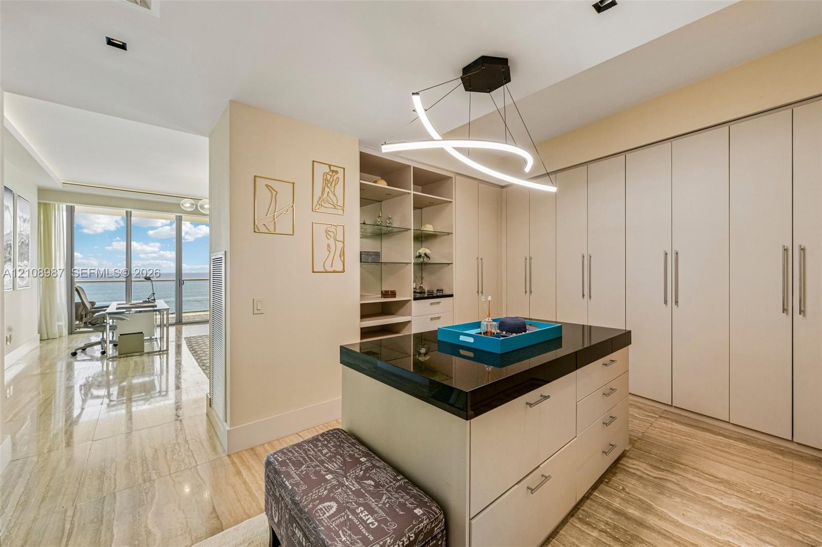 Custom storage cabinetry with integrated shelving, stone-topped central island, recessed lighting, contemporary geometric pendant fixture, and polished stone-finish flooring