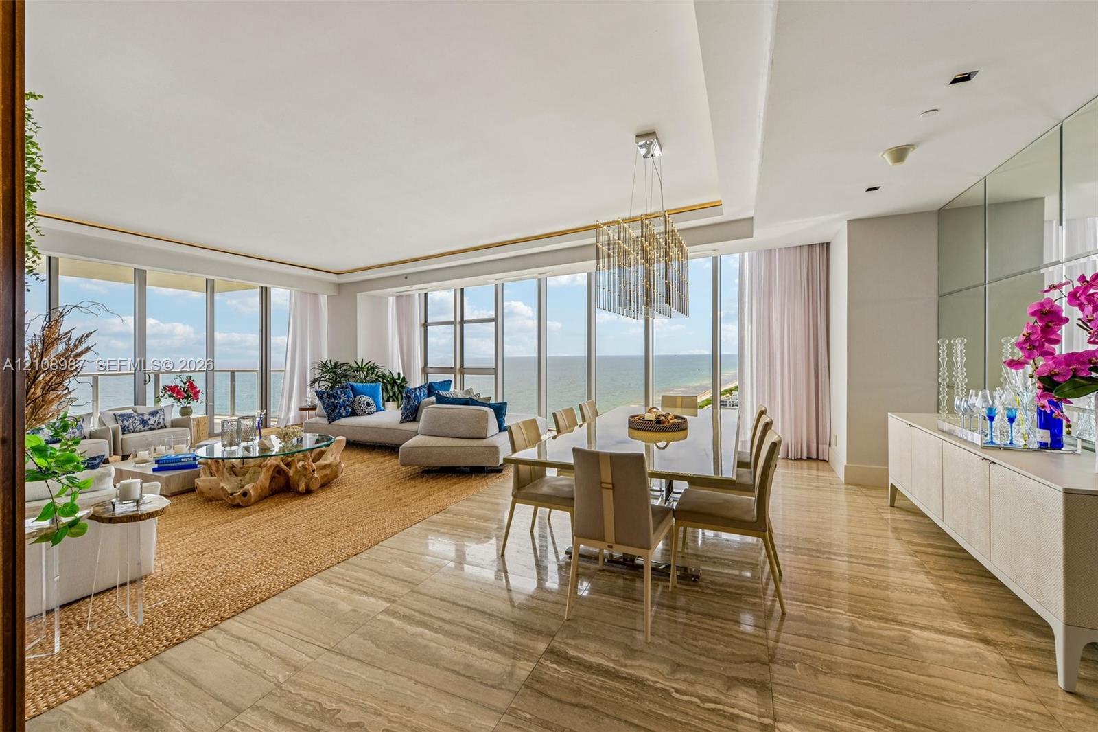 Floor-to-ceiling glass windows, stone flooring, integrated tray ceiling with recessed lighting, mirrored wall paneling, and rectangular tiered chandelier Floor-to-ceiling glass windows, stone flooring, integrated tray ceiling with recessed lighting, mirrored wall paneling, and rectangular tiered chandelier