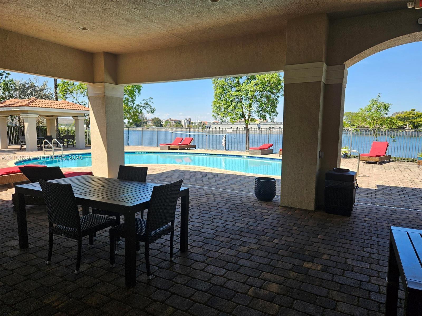 Covered brick-paver patio featuring a built-in swimming pool, detached gazebo, and metal fencing along the water