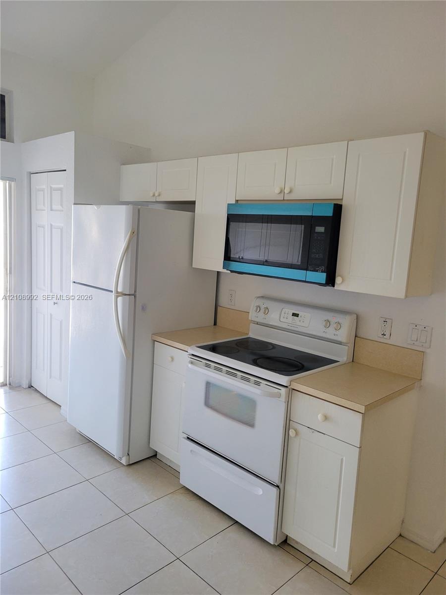 Kitchen featuring white cabinetry, light-toned countertops, a full-sized white refrigerator, a white electric range, an over-the-range microwave, and ceramic tile flooring