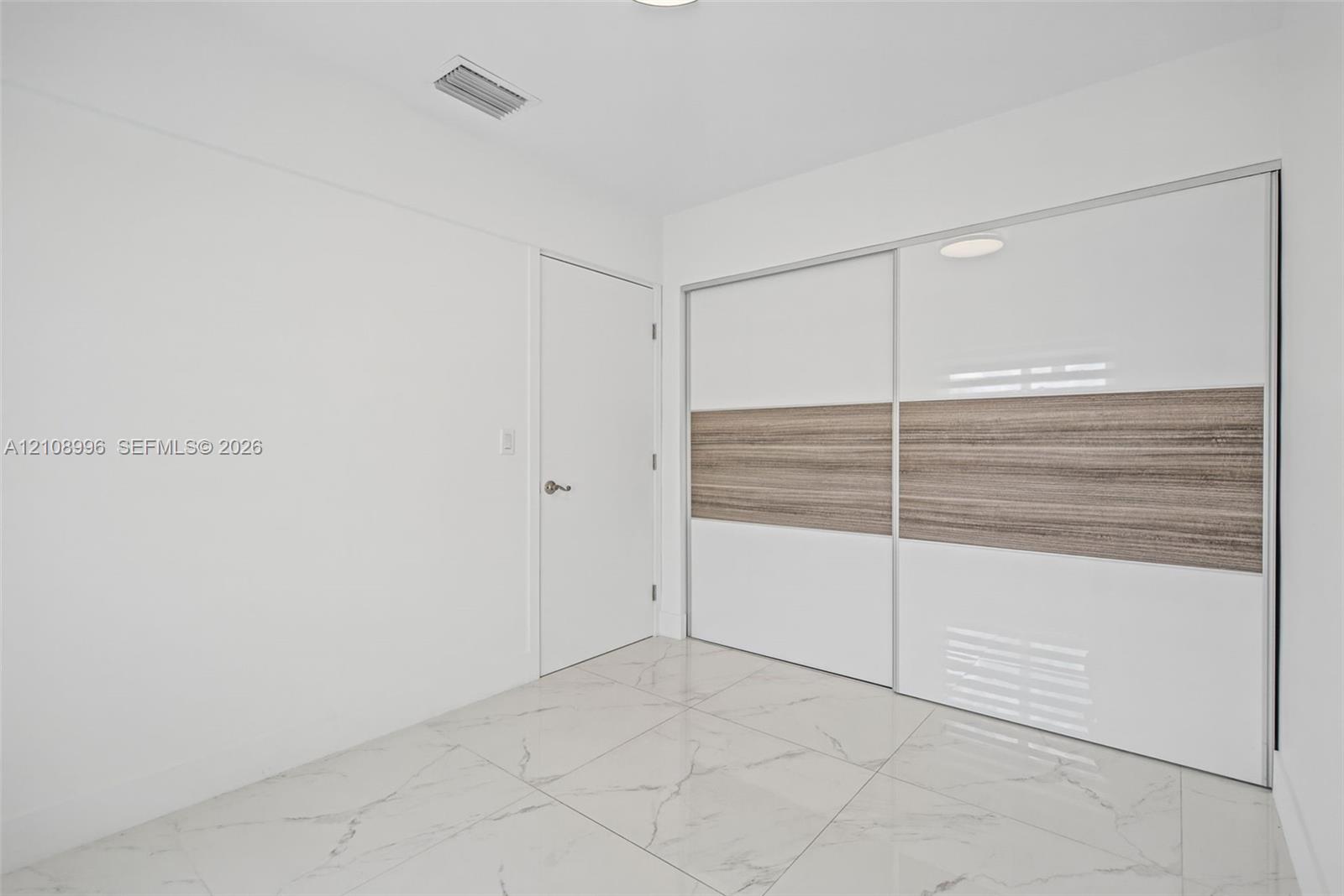 Large-format polished tile flooring featuring a veined pattern, dual sliding closet doors with high-gloss white and wood-finish detailing, and a solid-core interior door