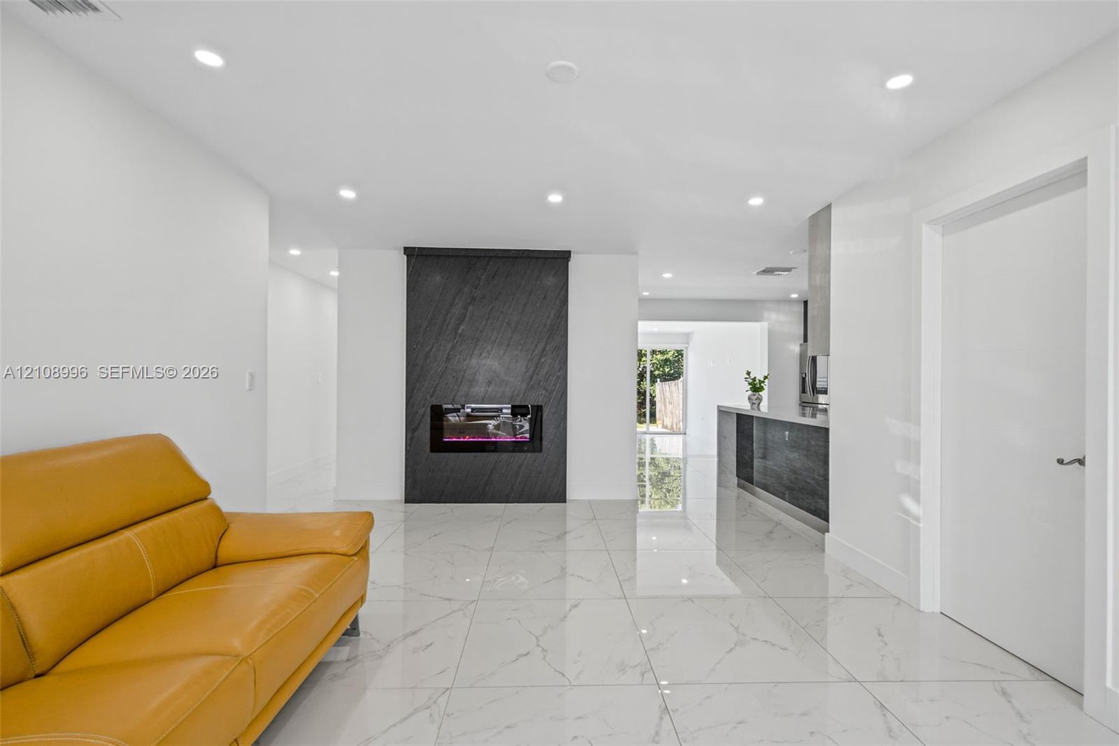Full-height dark stone fireplace feature, recessed LED lighting, white large-format tile flooring, and sleek built-in kitchen cabinetry