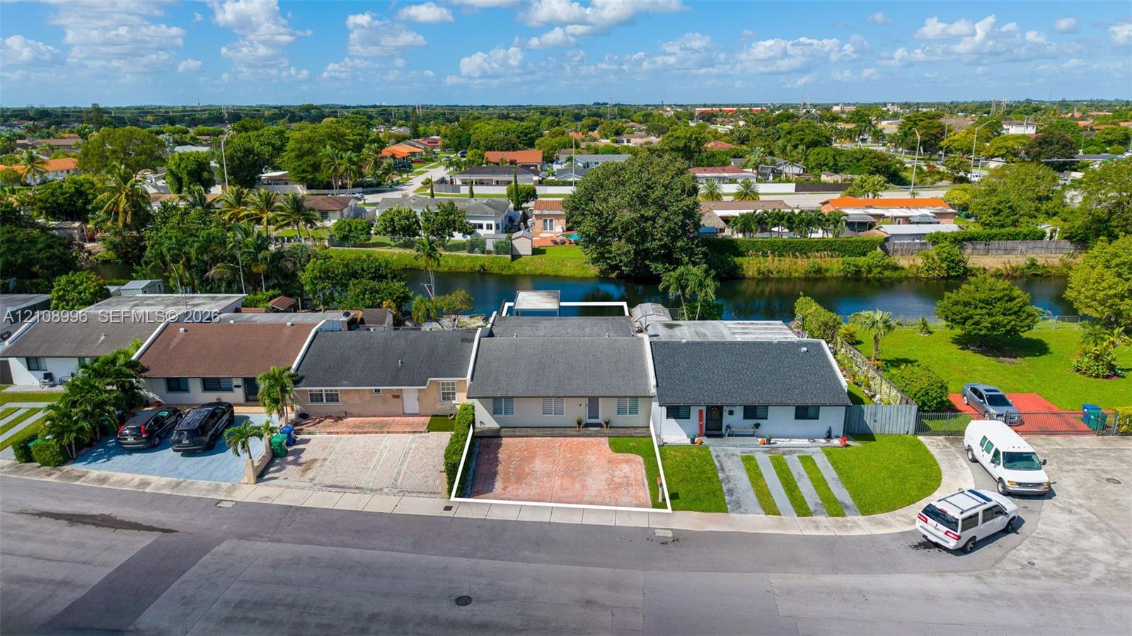 Aerial perspective of a single-story residence featuring a shingled roof, a paved front courtyard, and direct canal frontage with a manicured rear lawn
