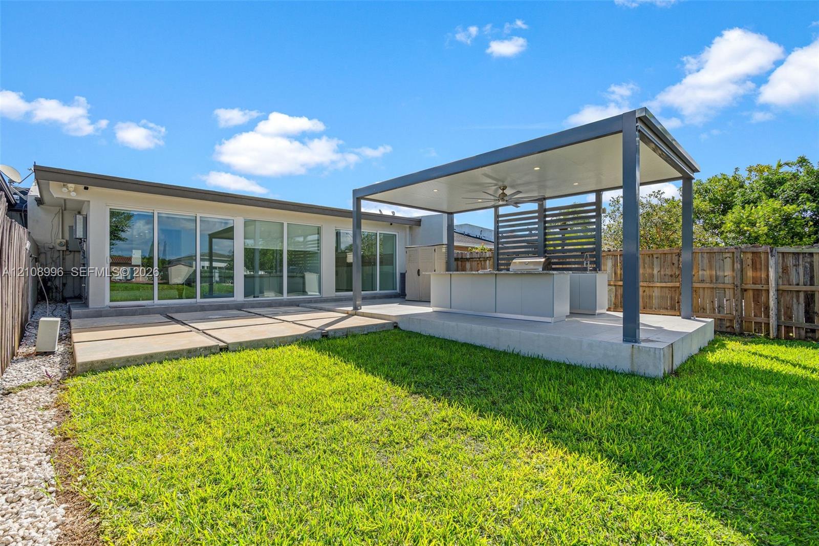 Backyard featuring a covered patio with a built-in outdoor kitchen, recessed ceiling lighting, a ceiling fan, and large-format concrete pavers