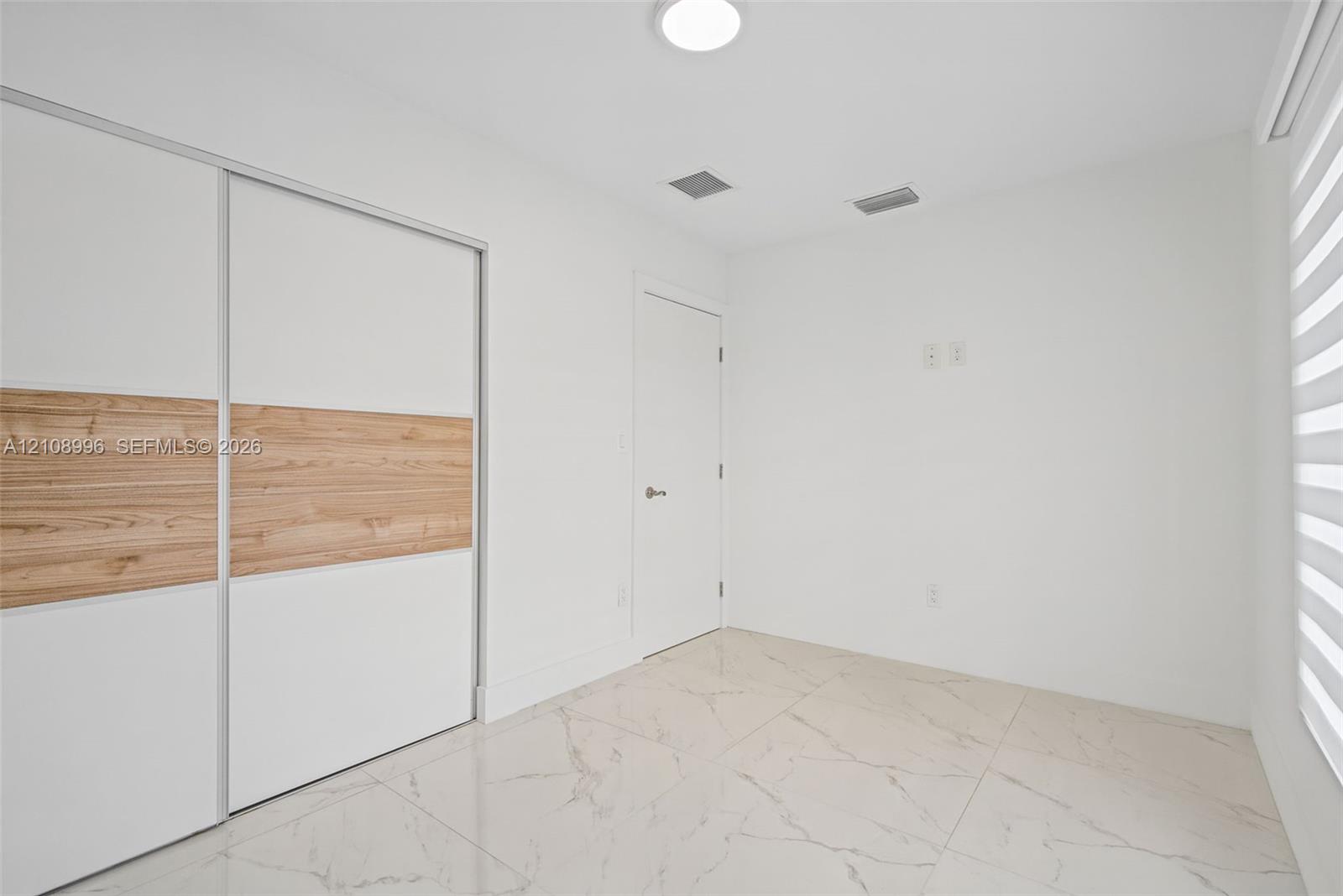 Large-format tile flooring with veining, sliding closet doors with wood-finish accents, and layered window shades