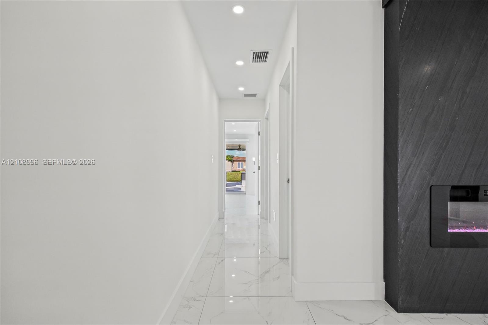 Hallway featuring large-format stone-look porcelain tile flooring, recessed ceiling lighting, and a floor-to-ceiling charcoal-toned stone fireplace surround with a built-in linear electric insert