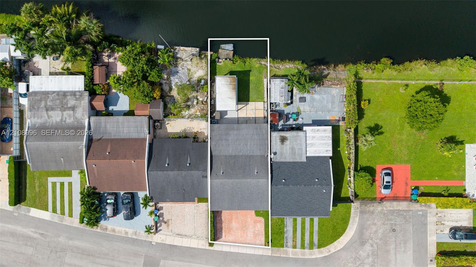 Waterfront property featuring a canal-front parcel, paved driveway, concrete rear patio, and fenced lawn area