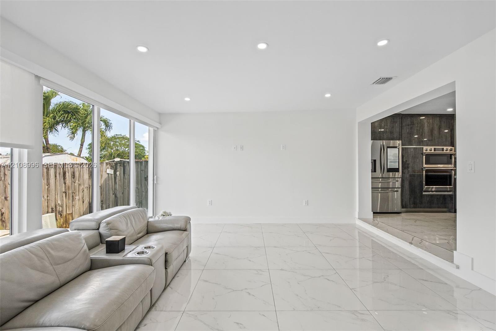 Large-format porcelain tile flooring, recessed ceiling lighting, and expansive floor-to-ceiling windows featuring exterior greenery