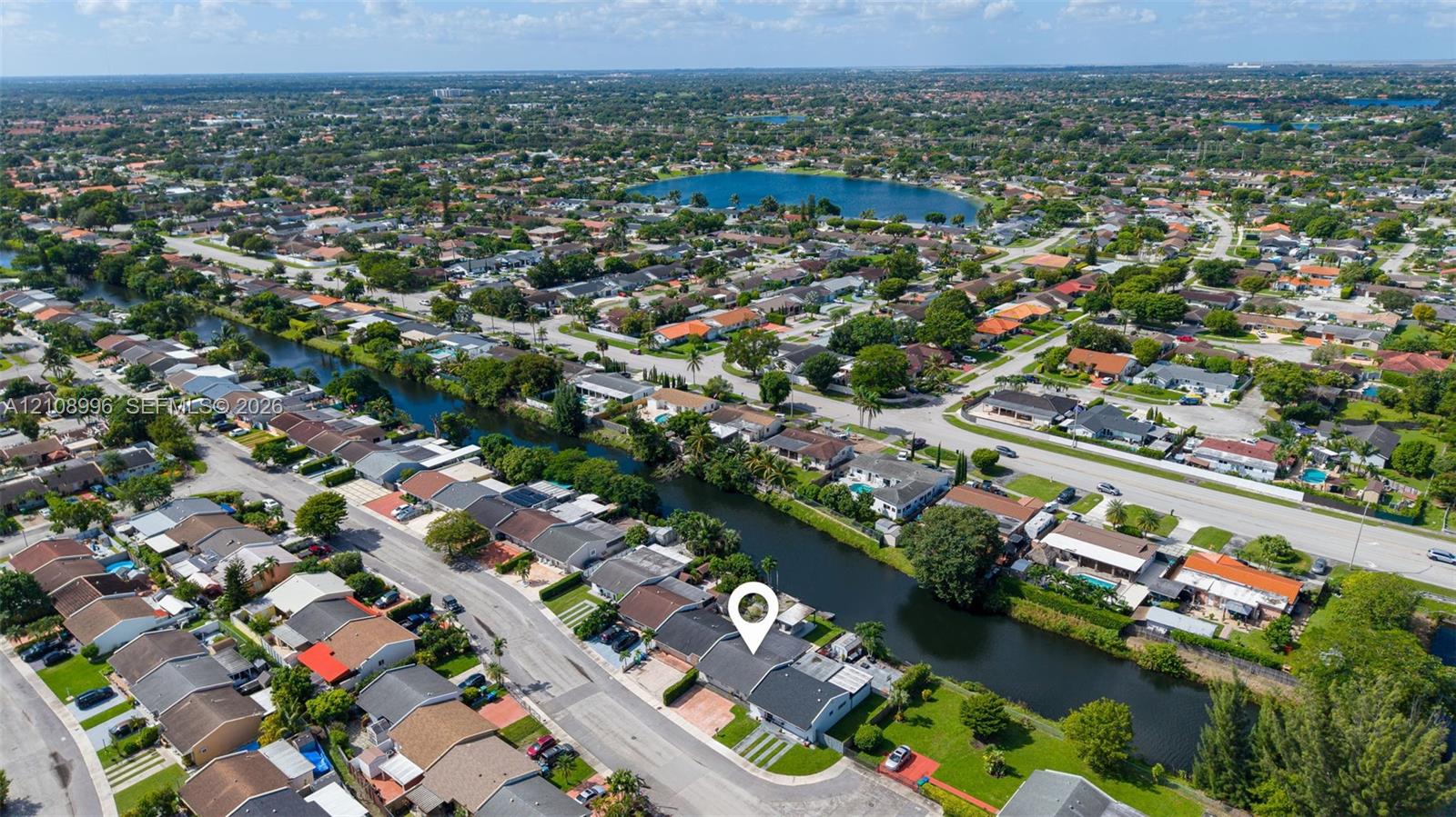 Aerial perspective of a single-story residence featuring a concrete tile roof, paved driveway, and direct water frontage along a canal