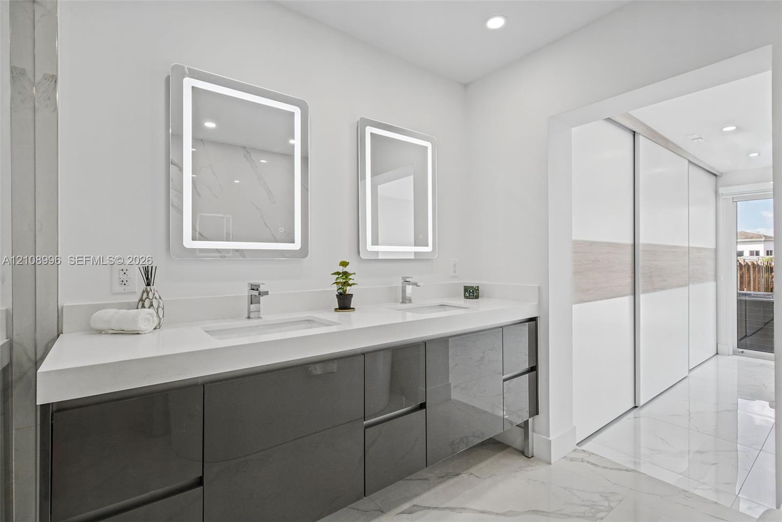 Dual-sink vanity featuring high-gloss charcoal cabinetry, white quartz countertop, integrated LED-backlit mirrors, and large-format tile flooring
