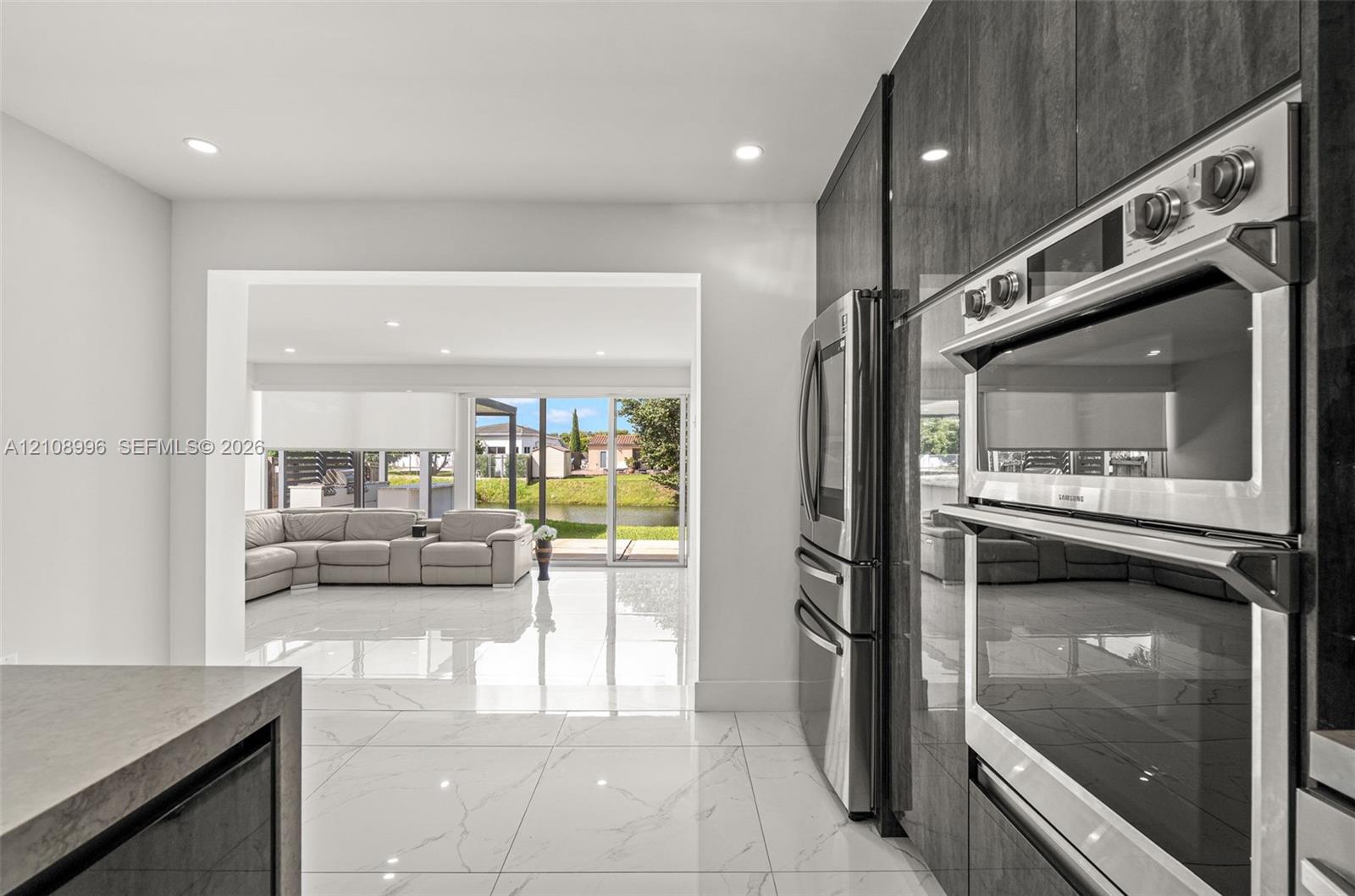 Modern kitchen featuring sleek, high-gloss charcoal cabinetry, integrated stainless steel double wall ovens, a stainless steel refrigerator, and large-format porcelain tile flooring