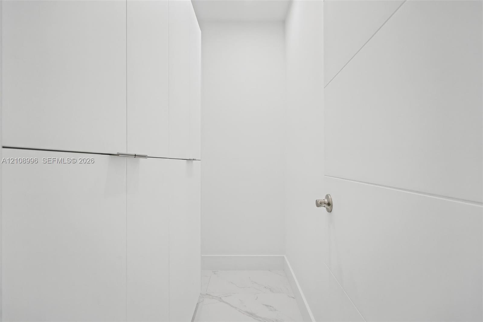 Built-in floor-to-ceiling cabinetry featuring clean-lined, white panel doors with minimalist hardware and white stone-finish tile flooring