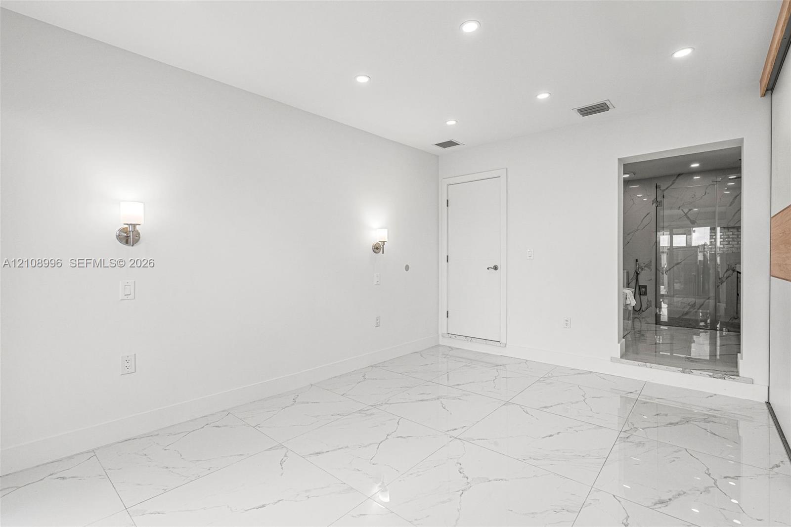 Large-format tile flooring with veined detailing, recessed ceiling lighting, and dual wall-mounted light fixtures