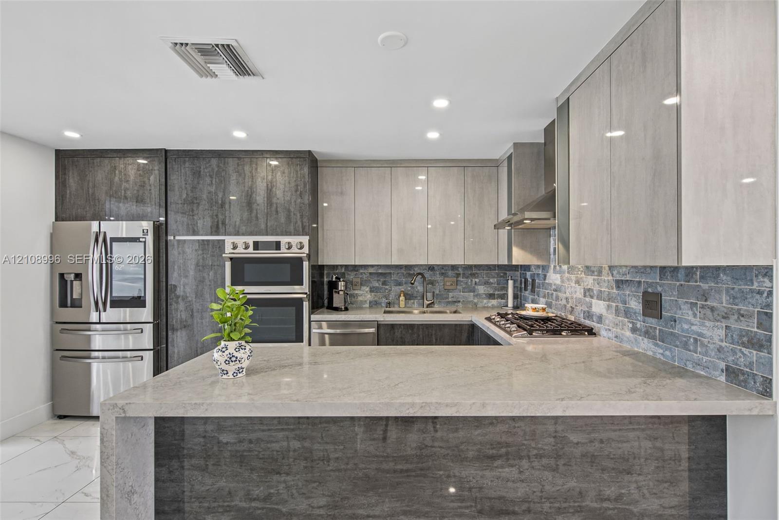 Modern kitchen featuring two-tone high-gloss cabinetry, stone countertops with waterfall edge, stainless steel built-in double wall ovens, and a decorative tile backsplash
