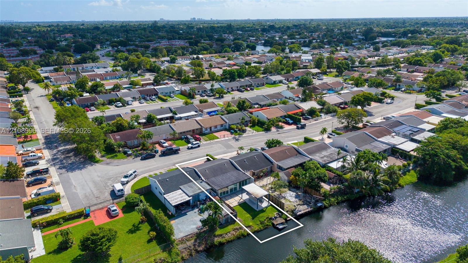 Waterfront property featuring a canal-side bulkhead, concrete patio, lawn area, and a metal-frame pergola