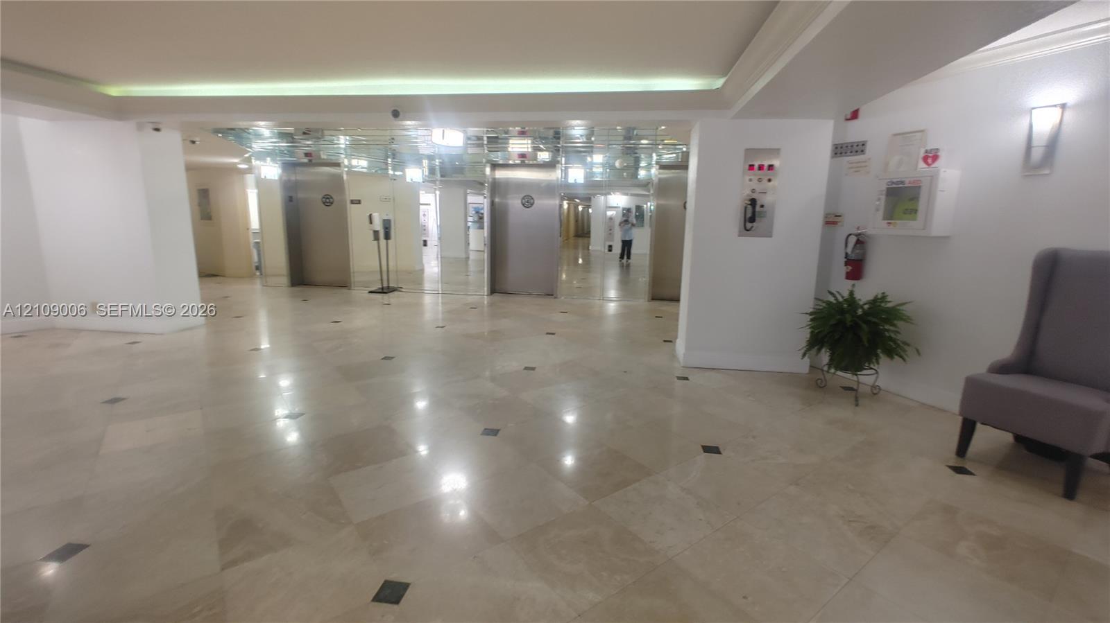 Lobby featuring polished stone flooring with inlaid tile accents, stainless steel elevator doors, mirrored wall paneling, and recessed ceiling lighting