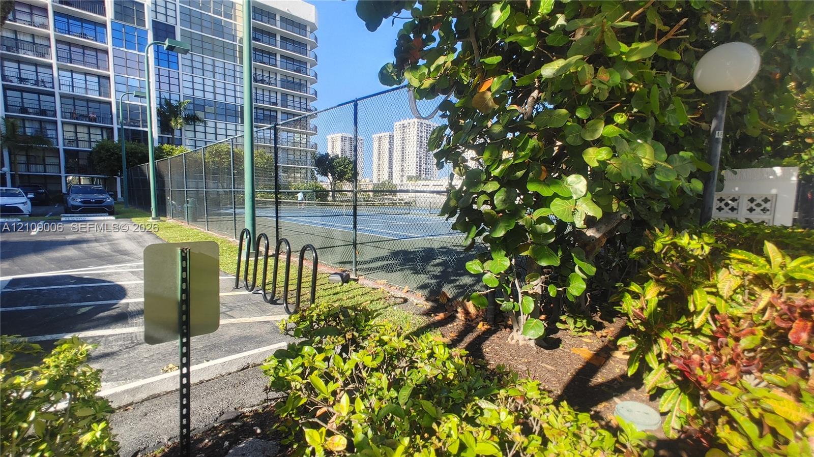Tennis court enclosed by chain-link fencing, accompanied by a dedicated bicycle rack and exterior landscape lighting