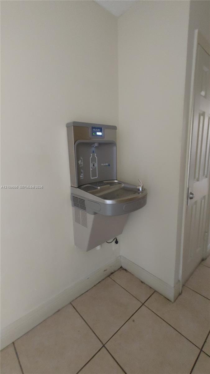 Wall-mounted stainless steel bottle filling station and water fountain with a digital filter monitor and tile flooring