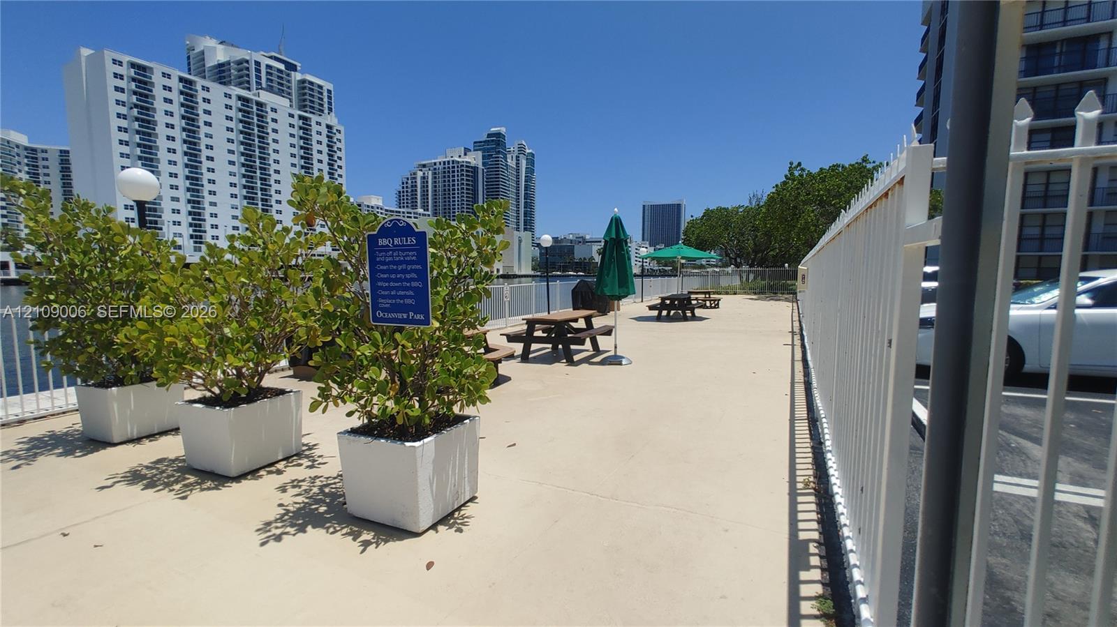 Outdoor recreation area featuring paved hardscaping, perimeter metal fencing, and decorative planter boxes