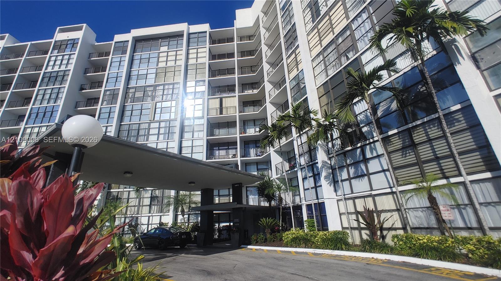 High-rise building exterior featuring a covered porte-cochre, multi-level glass balconies, and manicured tropical landscaping
