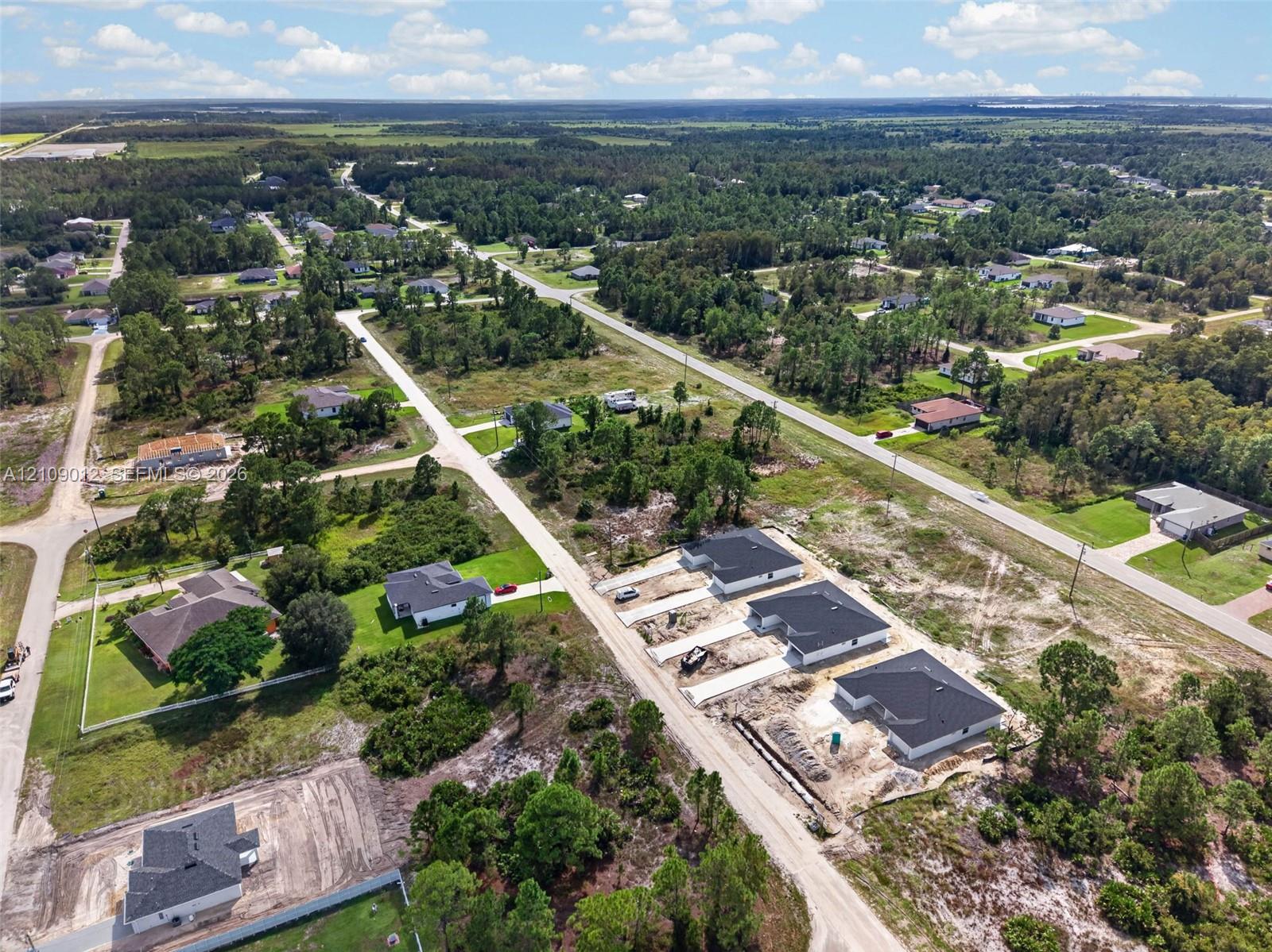 Aerial perspective of a residential development featuring paved roadways, single-family structures, and cleared lots surrounded by dense tree lines