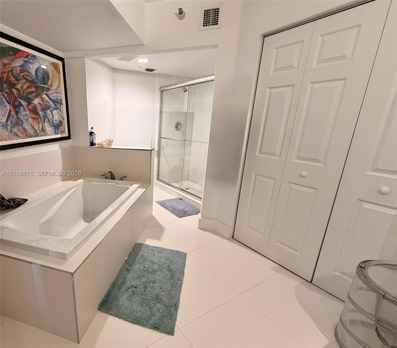 Bathroom featuring a drop-in soaking tub, a glass-enclosed shower, large-format tile flooring, and dual bi-fold closet doors