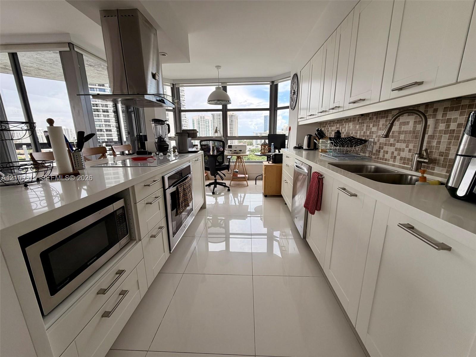 Kitchen featuring white cabinetry, quartz countertops, stainless steel appliances, a mosaic tile backsplash, and large-format porcelain floor tiling Kitchen featuring white cabinetry, quartz countertops, stainless steel appliances, a mosaic tile backsplash, and large-format porcelain floor tiling