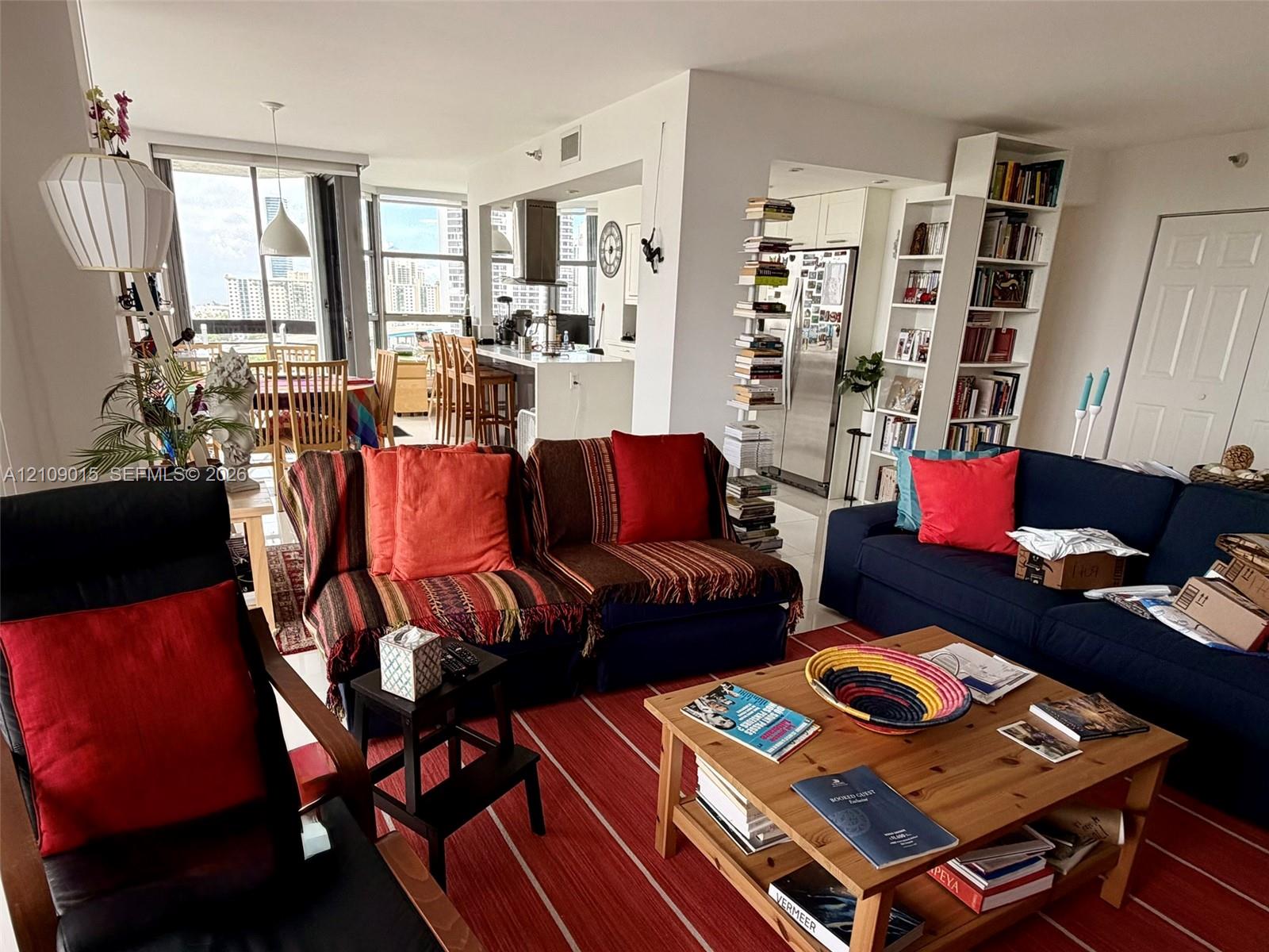 Open-concept floor plan featuring floor-to-ceiling windows, built-in floor-to-ceiling shelving, stainless steel kitchen appliances, and a kitchen island with stone-surface countertop Open-concept floor plan featuring floor-to-ceiling windows, built-in floor-to-ceiling shelving, stainless steel kitchen appliances, and a kitchen island with stone-surface countertop