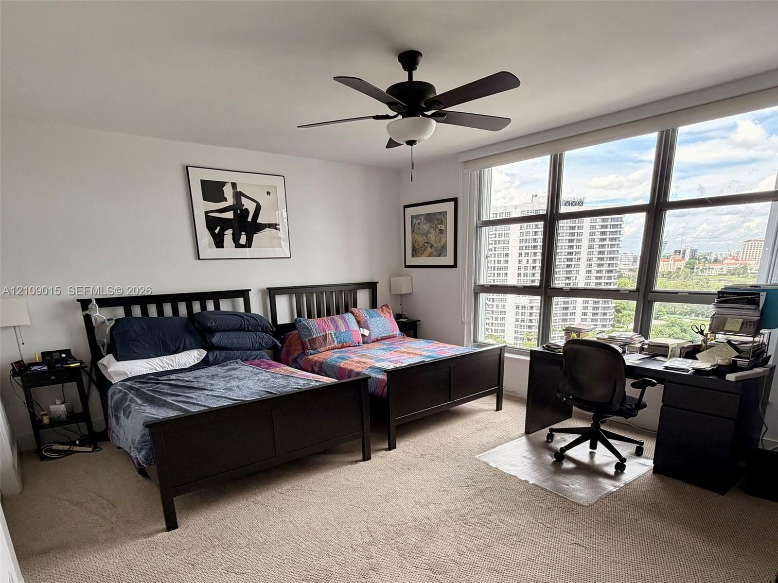 Bedroom featuring neutral carpeting, floor-to-ceiling windows with grid framing, and a matte black ceiling fan with integrated lighting