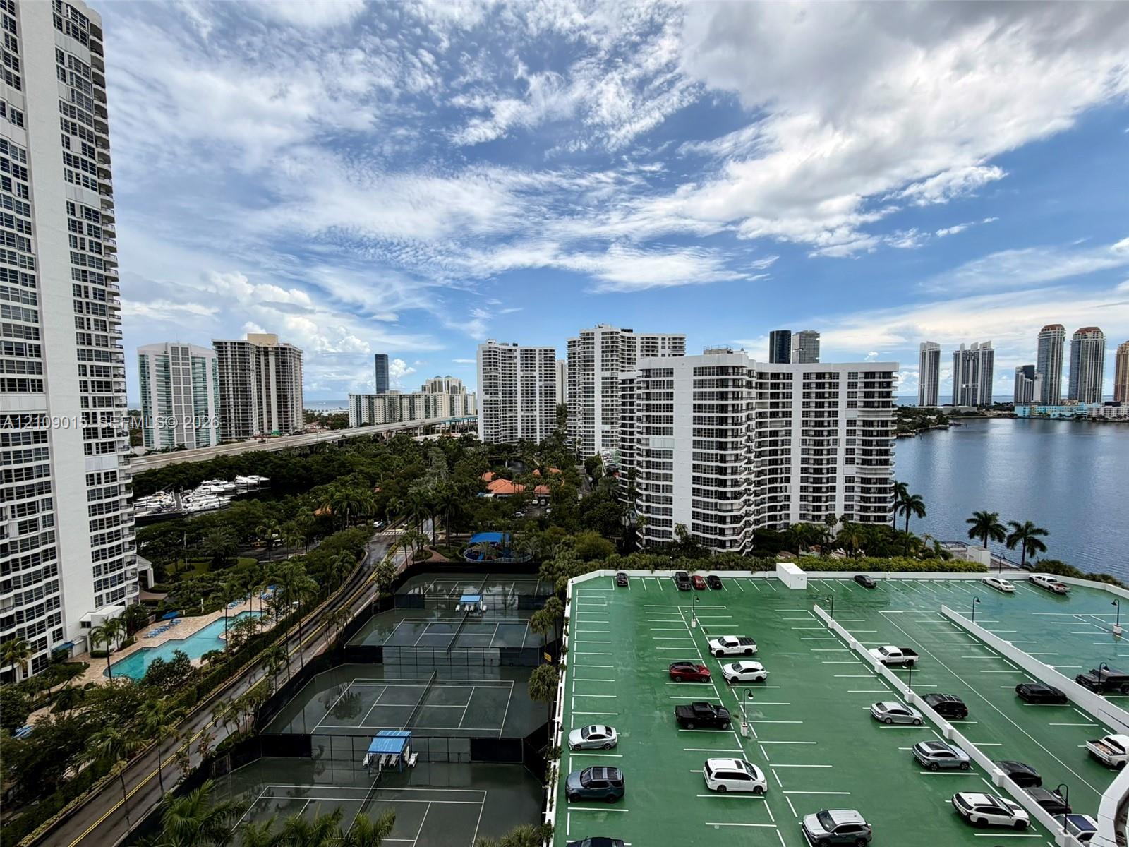 High-rise perspective featuring tennis courts, a surface parking structure, and proximity to an expansive waterfront canal and urban skyline