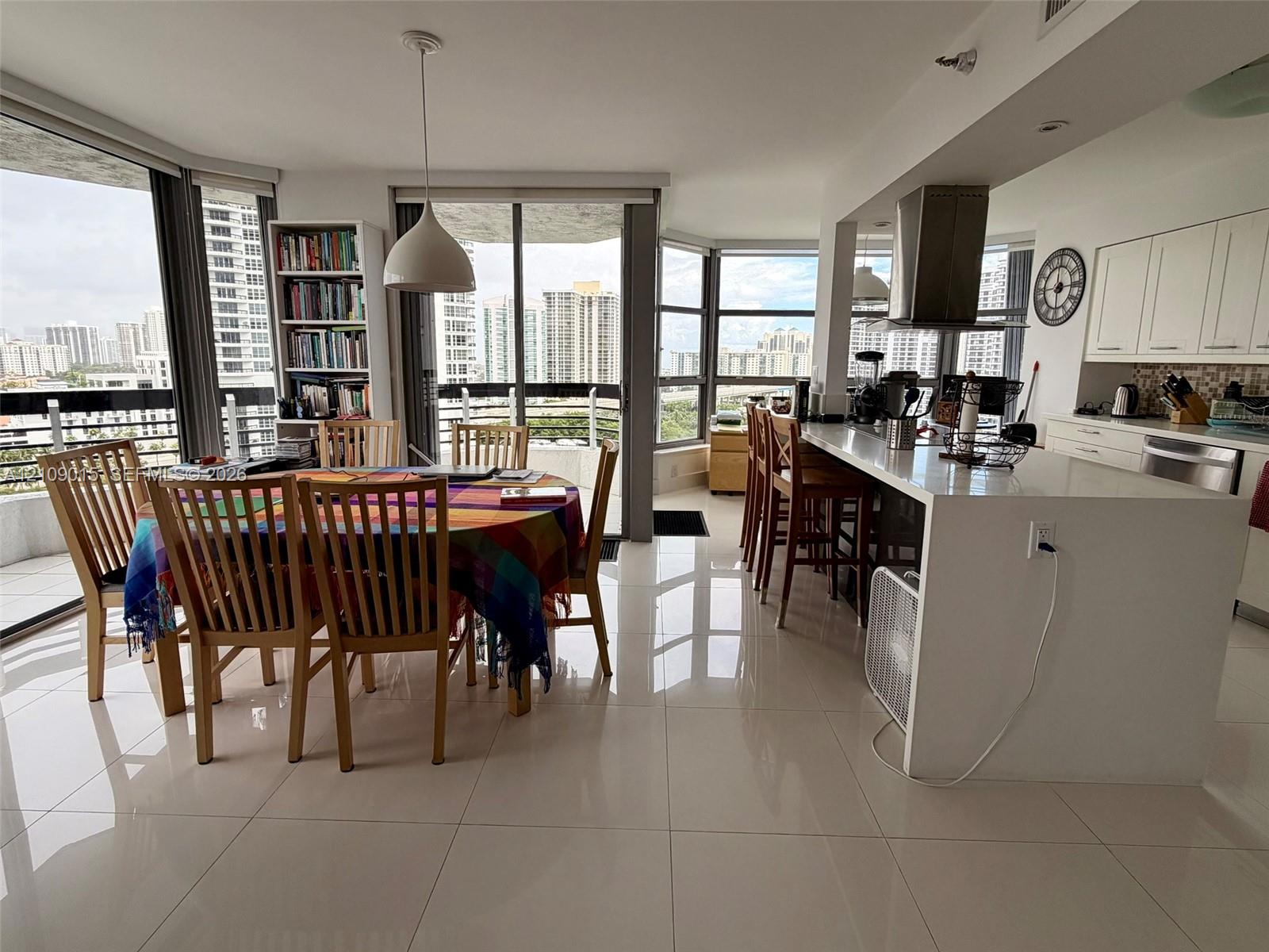 Open-concept interior featuring large-format tile flooring, floor-to-ceiling windows, white cabinetry, a quartz waterfall-edge kitchen island, and a stainless steel range hood Open-concept interior featuring large-format tile flooring, floor-to-ceiling windows, white cabinetry, a quartz waterfall-edge kitchen island, and a stainless steel range hood