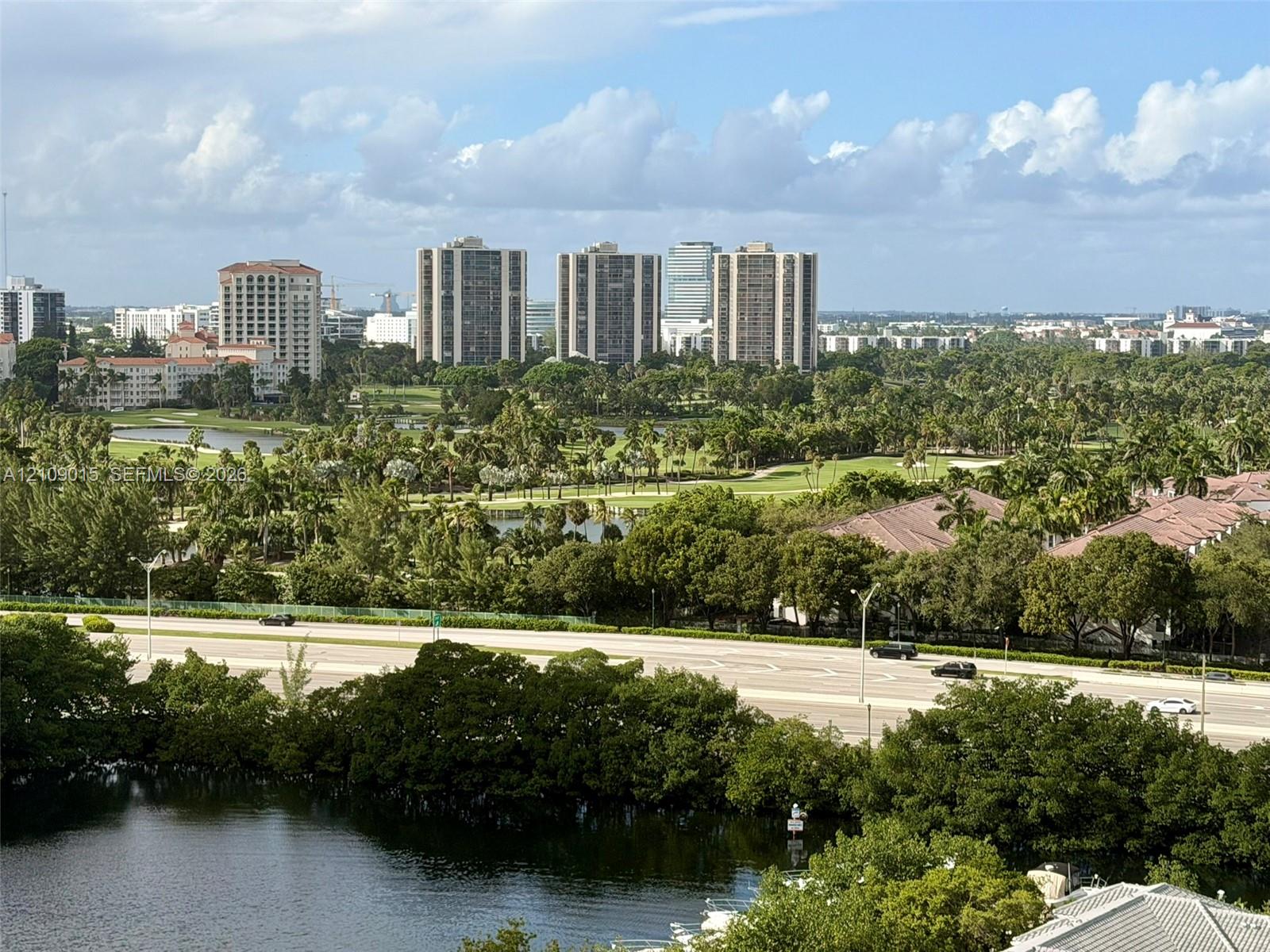 Panoramic landscape featuring golf course grounds, mature tree canopy, natural water features, and high-rise skyline