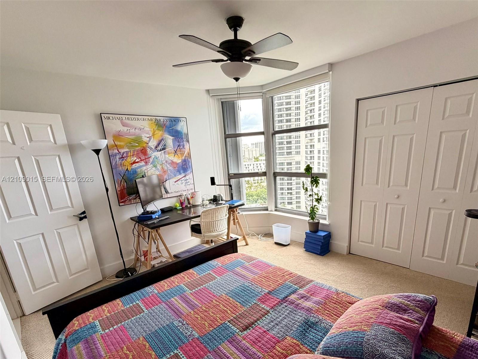 Bay window with floor-to-ceiling glass, neutral carpeting, ceiling fan with integrated light fixture, and white dual-panel closet doors