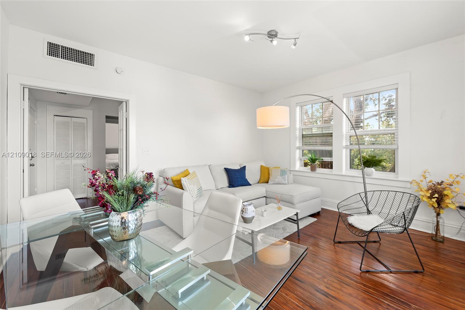 Living area featuring wood-finish flooring, two large windows with white trim, and a multi-directional track lighting fixture