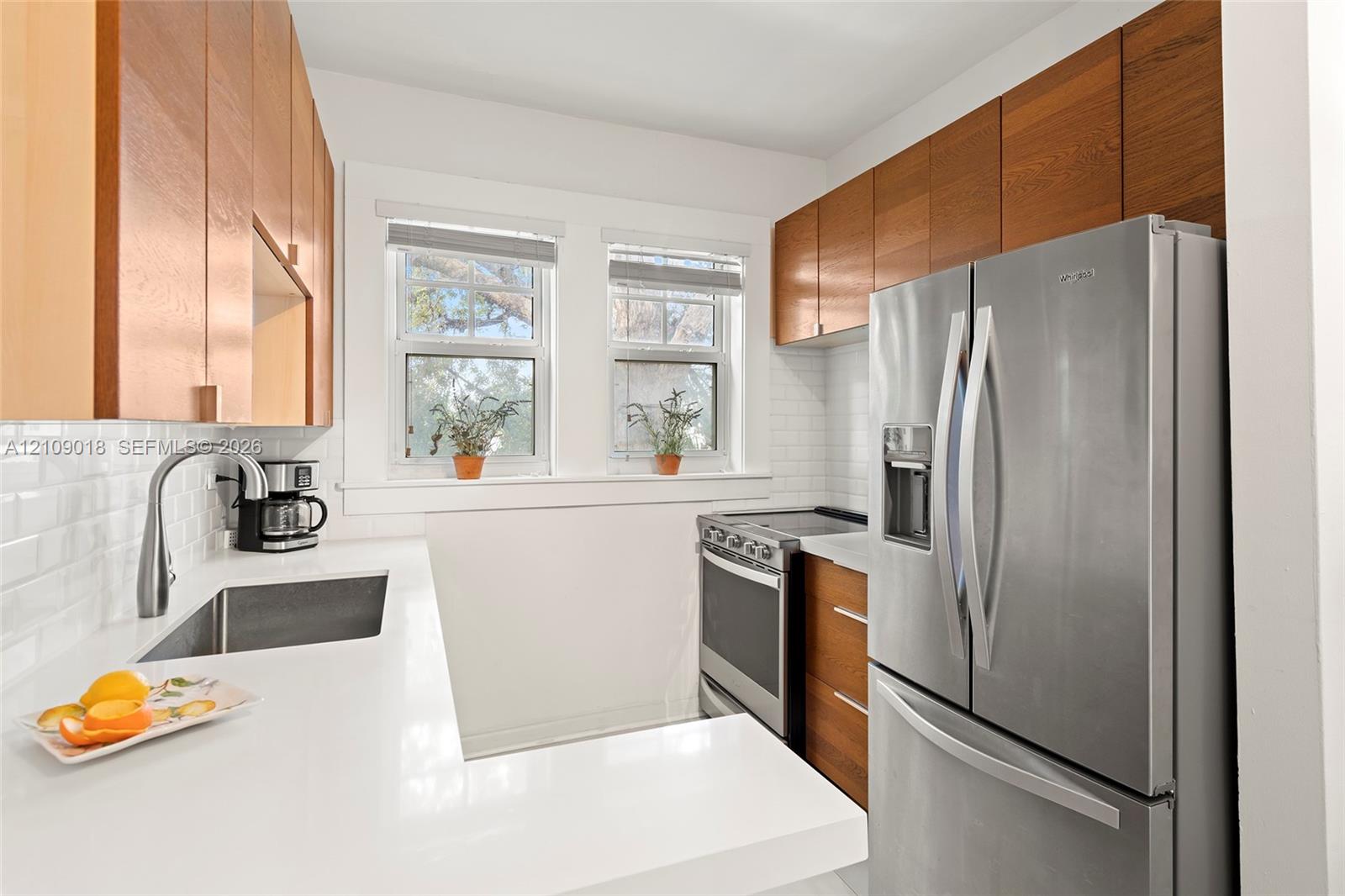 Kitchen featuring wood-finish cabinetry, white solid-surface countertops, subway tile backsplash, stainless steel appliances, and a stainless steel undermount sink with a gooseneck faucet